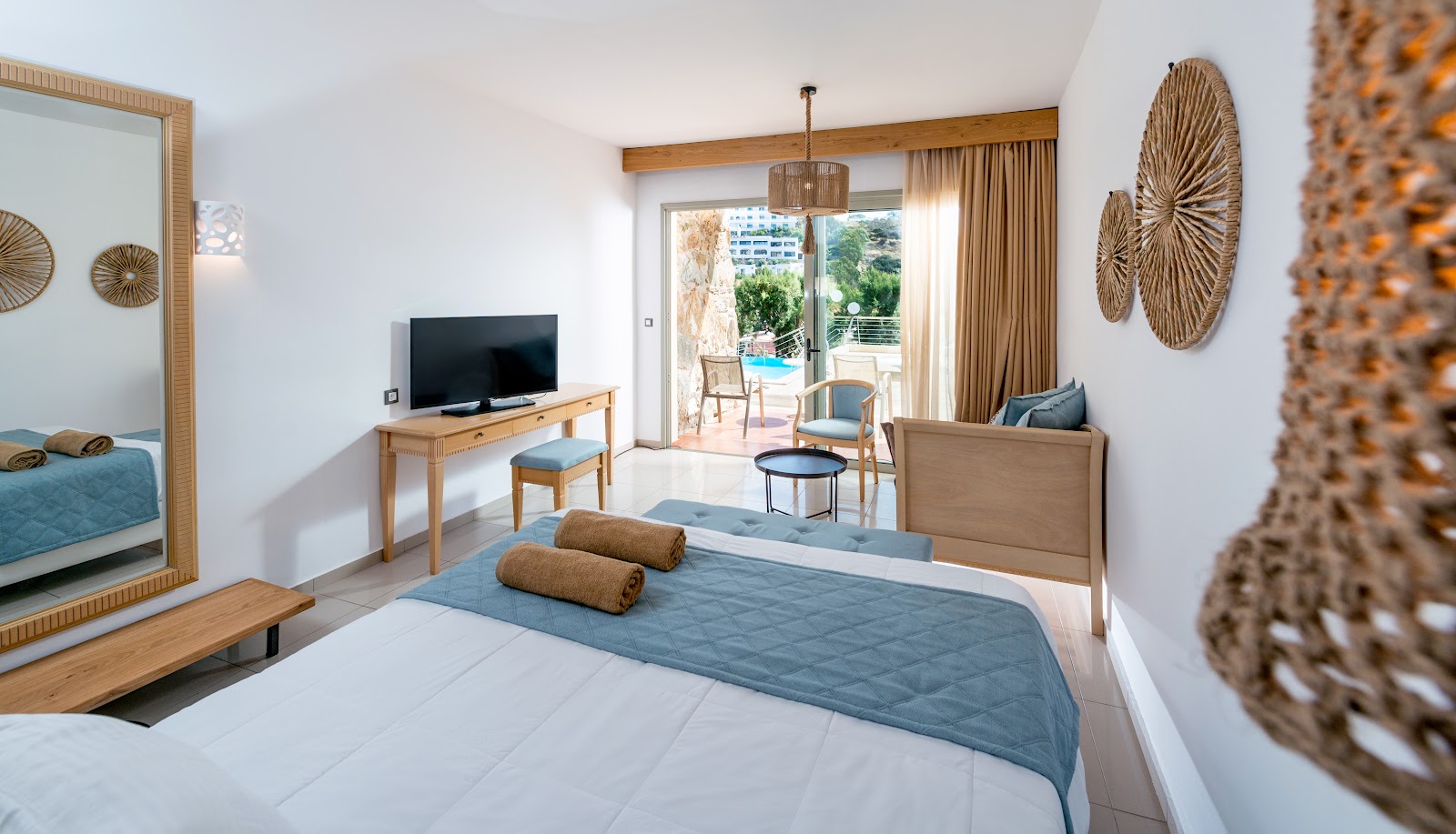 Spacious resort bedroom with wooden canopy bed, hanging chair, and floor-to-ceiling windows overlooking a balcony at Sea Side A Lifestyle Resort.