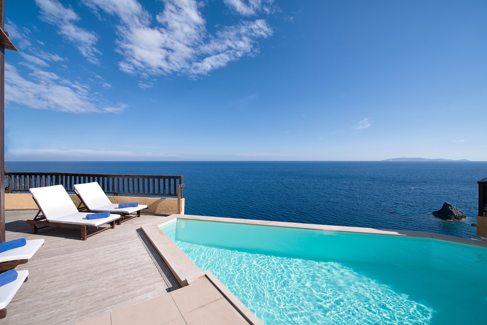 Infinity pool overlooking the deep blue Aegean Sea at Sea Side A Lifestyle Resort, with lounge chairs and wooden deck in foreground.