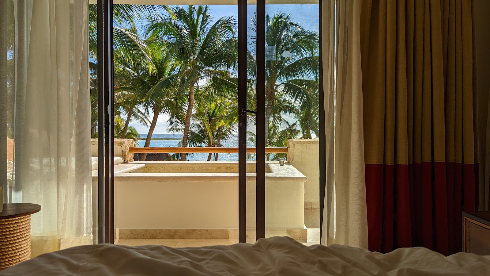 Beachfront bedroom at Secrets Akumal Riviera Maya with ocean view through glass doors, palm trees, and balcony.