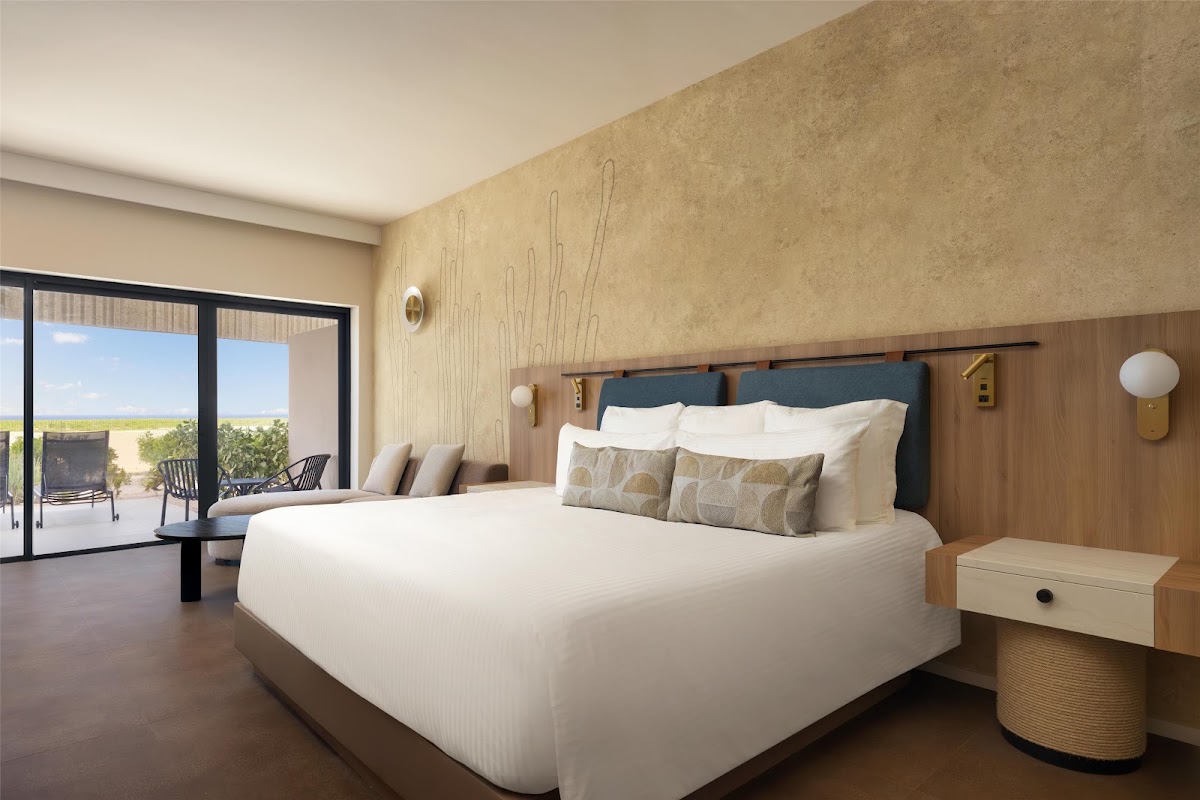 Modern resort bedroom with king bed, wood headboard, and sliding glass doors opening to a beachfront balcony at Secrets Baby Beach Aruba.