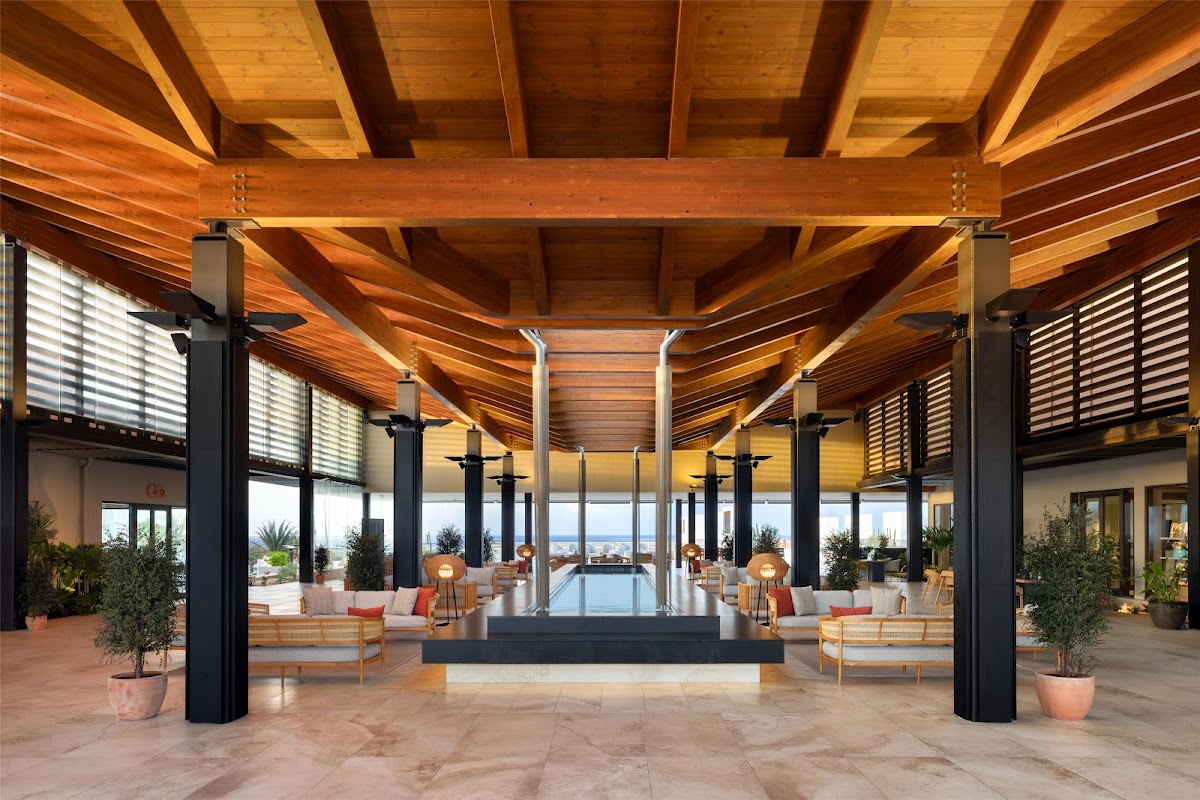 Spacious lobby with exposed wood beams, black support columns, lounge seating, and ocean views through floor-to-ceiling windows at Secrets Baby Beach Aruba.