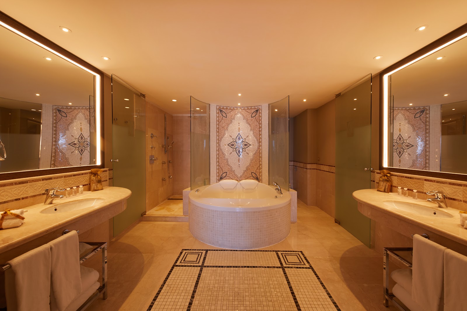 Luxury spa bathroom with dual vanities, illuminated mirrors, soaking tub, and walk-in shower with ornate tilework at Secrets Bahia Real Resort & Spa.