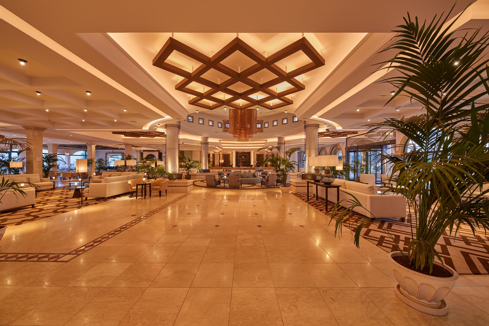 Buffet spread in an indoor dining room with colorful bowls, fresh pastries, beverages, and potted plants against wooden paneled walls with geometric patterns.