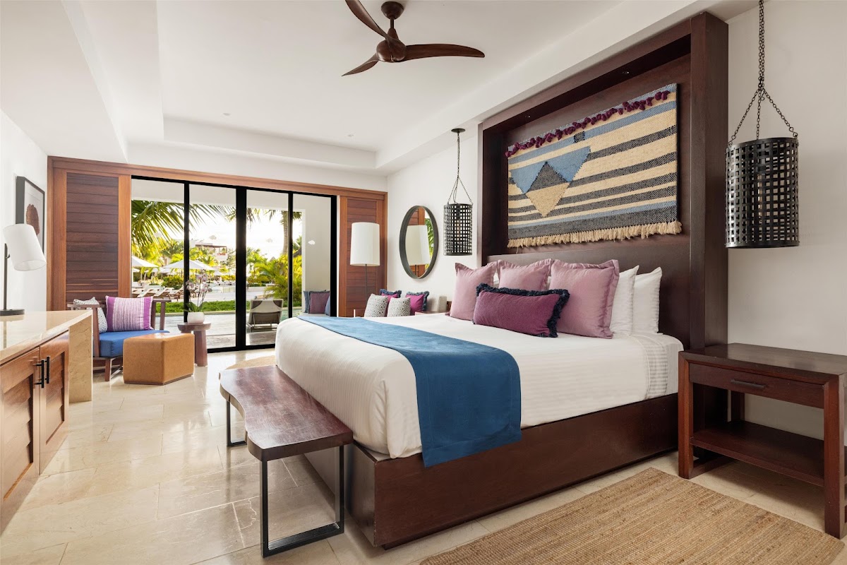 Spacious bedroom at Secrets Cap Cana Resort & Spa with king bed, dark wood headboard, and sliding glass doors overlooking tropical grounds.