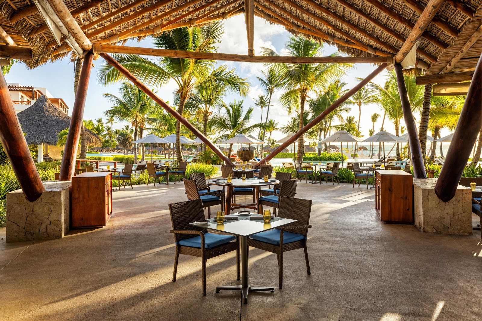 Beachfront balcony at Secrets Cap Cana with lounge seating, wooden pergola, and turquoise ocean beyond palm-lined white sand beach.