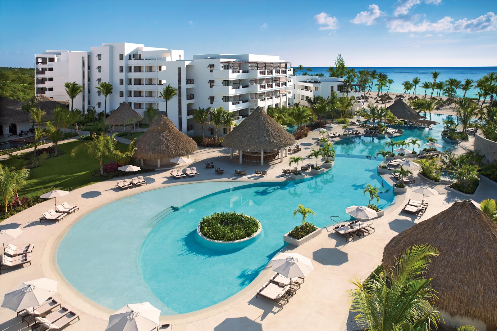Aerial view of Secrets Cap Cana Resort & Spa with beachfront, pool areas, thatched-roof structures, and multi-story hotel buildings surrounded by tropical vegetation.
