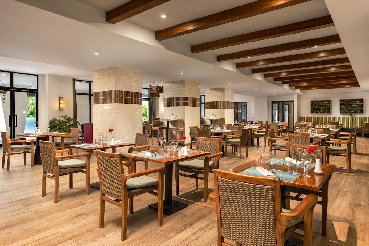 Dining room at Secrets Cap Cana Resort & Spa with wood tables, woven chairs, cream-colored columns, and exposed wooden ceiling beams.