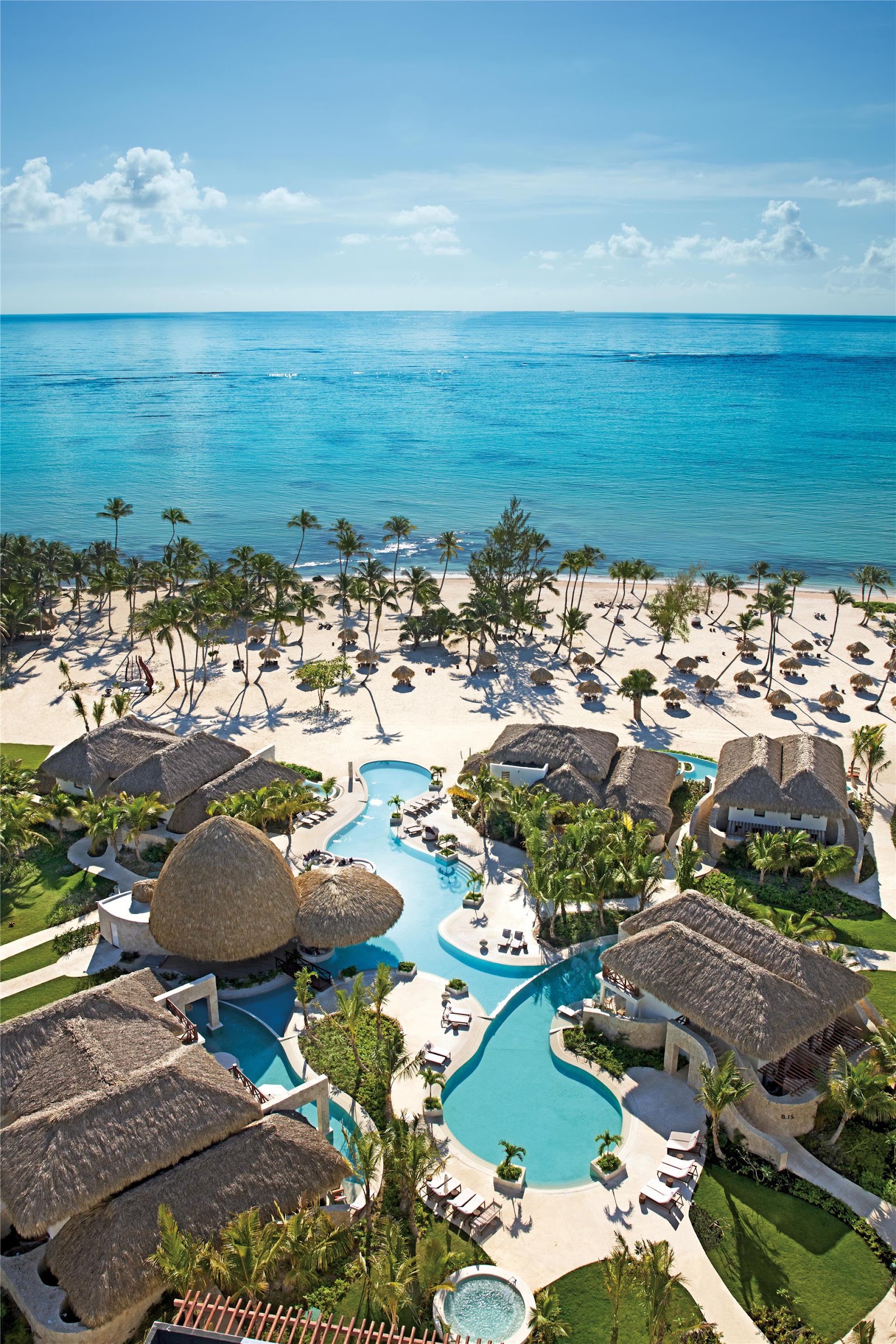 Dining pavilion with wooden beams and thatched roof overlooking palm trees, beach umbrellas, and ocean at Secrets Cap Cana Resort & Spa.