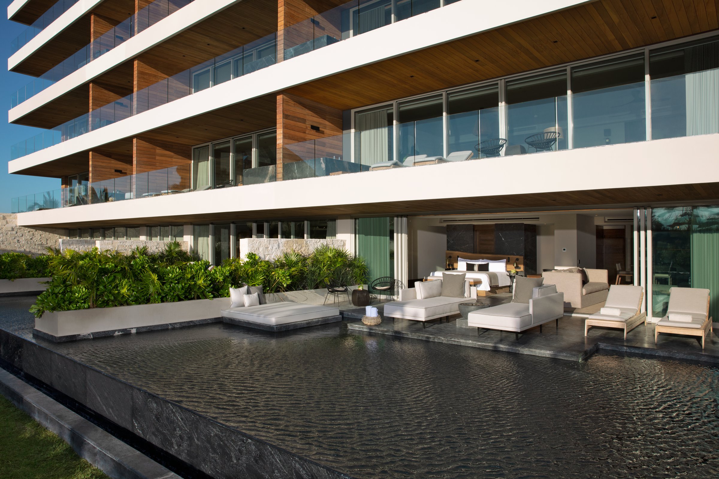 Swim-out suite terrace with white loungers beside a dark pool in front of a modern multi-story building.