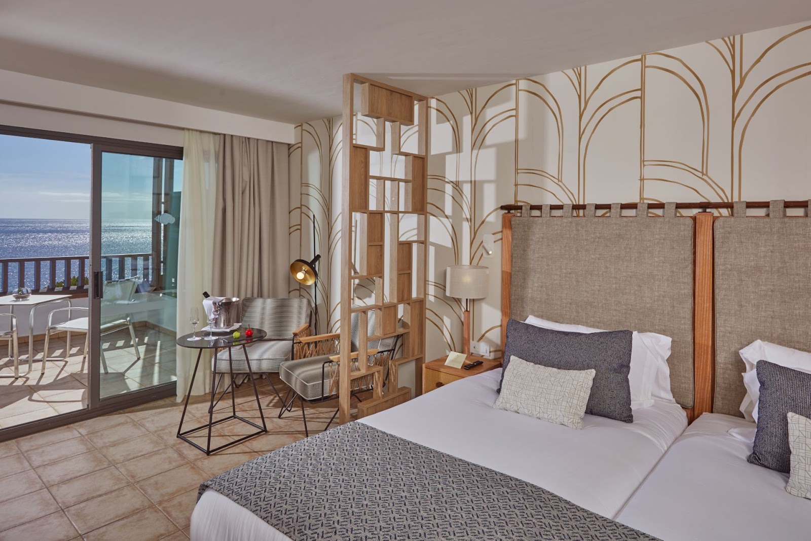 Modern hotel room with two beds, decorative wood room dividers, and ocean-view balcony at Secrets Lanzarote Resort & Spa.