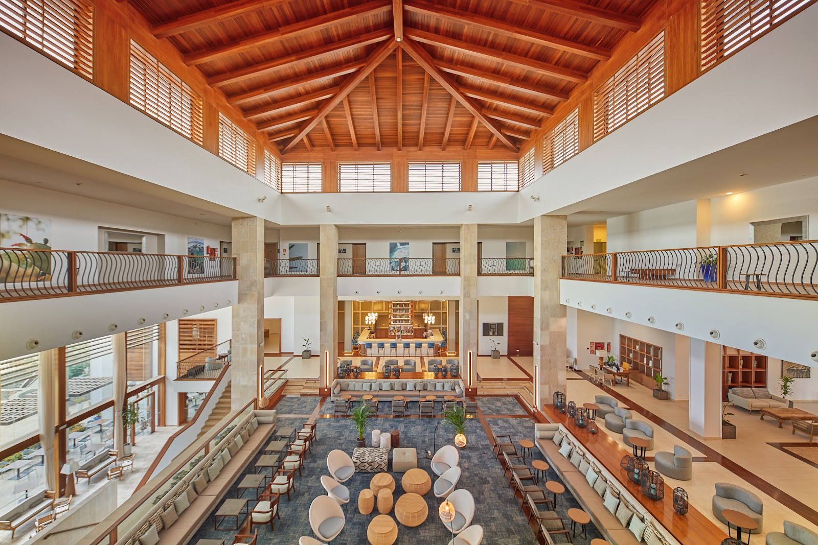 Expansive atrium with wooden ceiling beams, multiple balconied levels, and seating areas arranged around a central floor at Secrets Lanzarote Resort & Spa.
