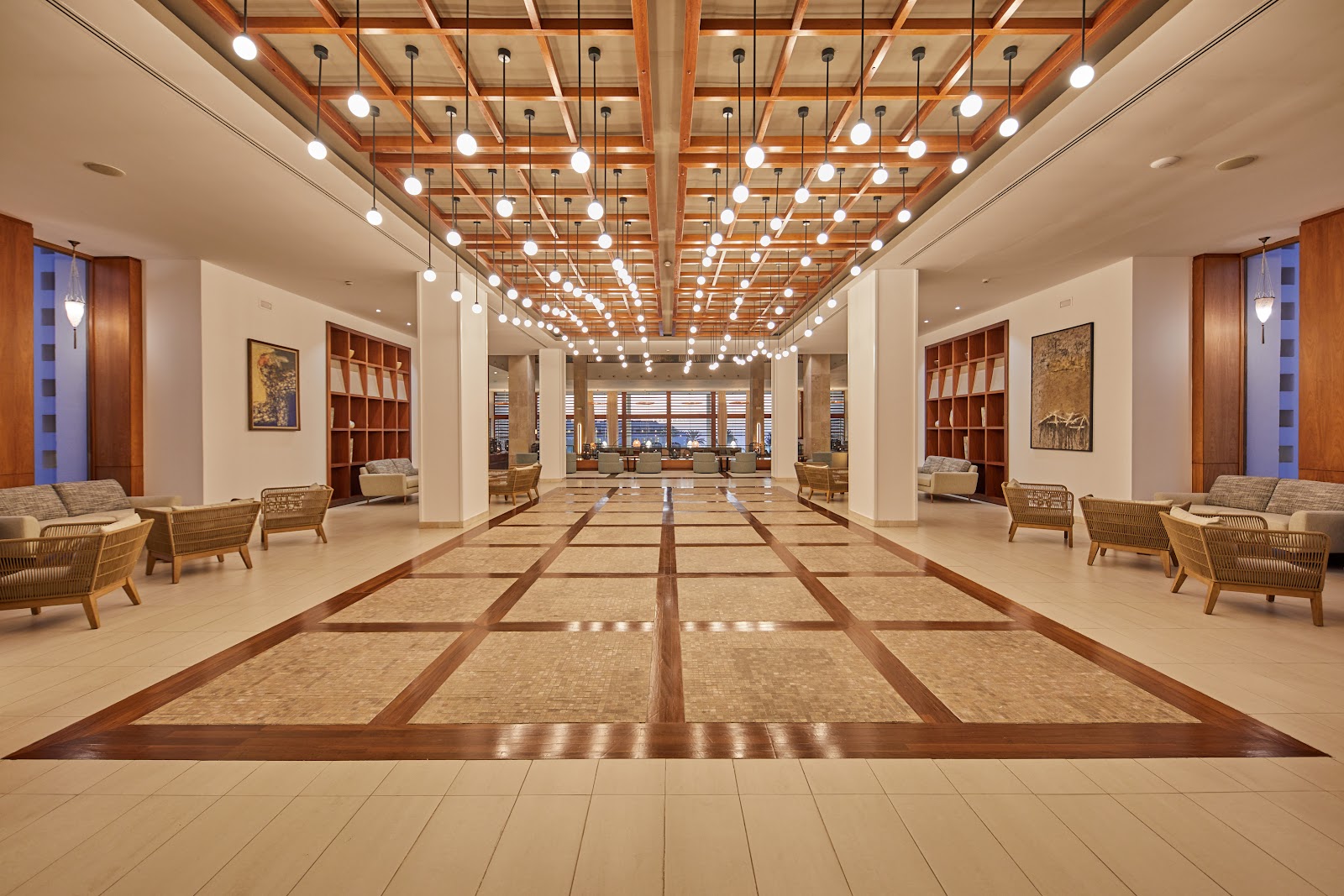 Spacious lobby with wooden ceiling beams, pendant lights, geometric floor inlay, wicker seating, and decorative wall shelving at Secrets Lanzarote Resort & Spa.