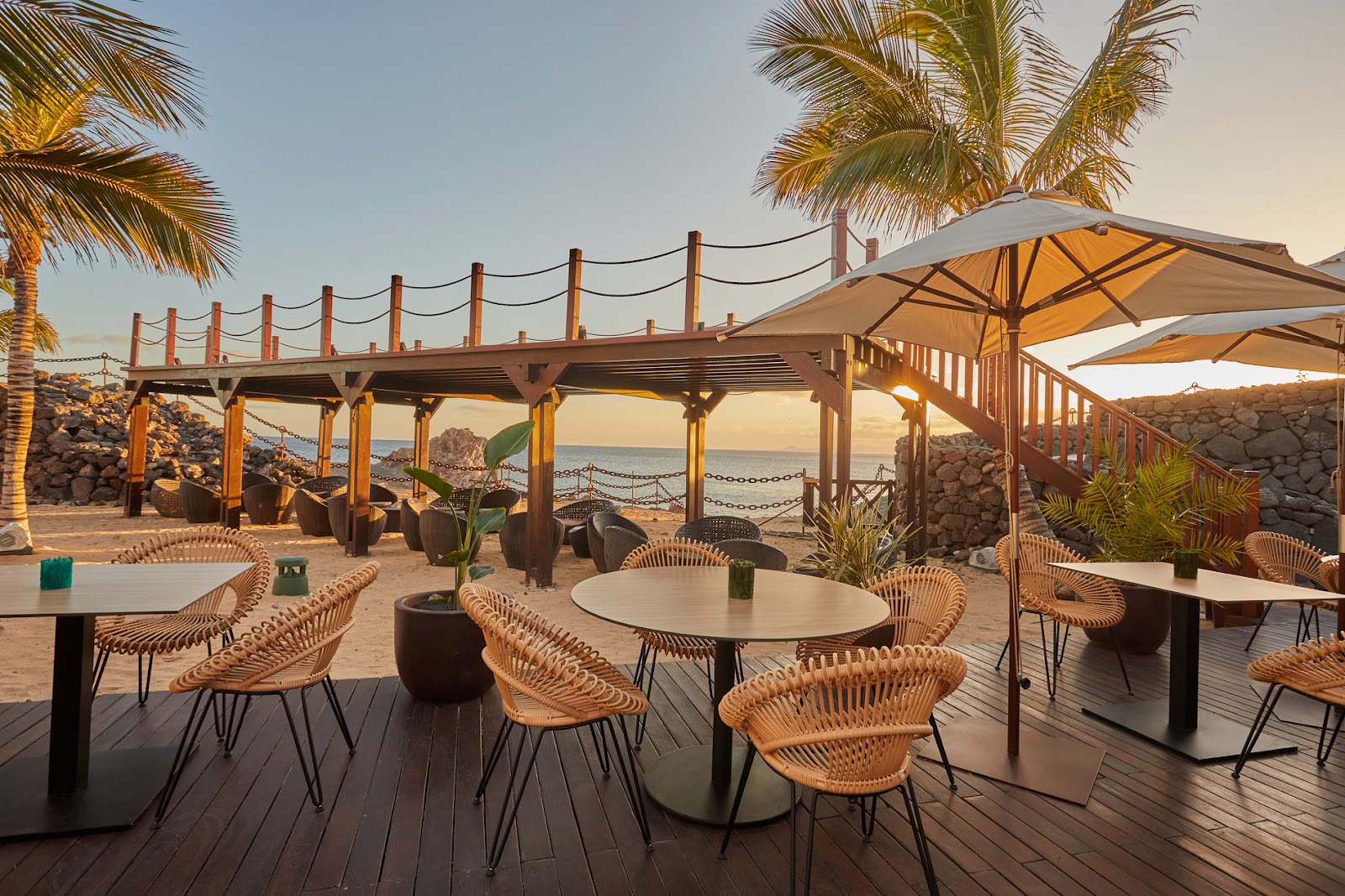 Contemporary dining room at Secrets Lanzarote Resort & Spa with wooden tables, light blue and navy chairs, pendant lights, and an open kitchen visible along the back wall.