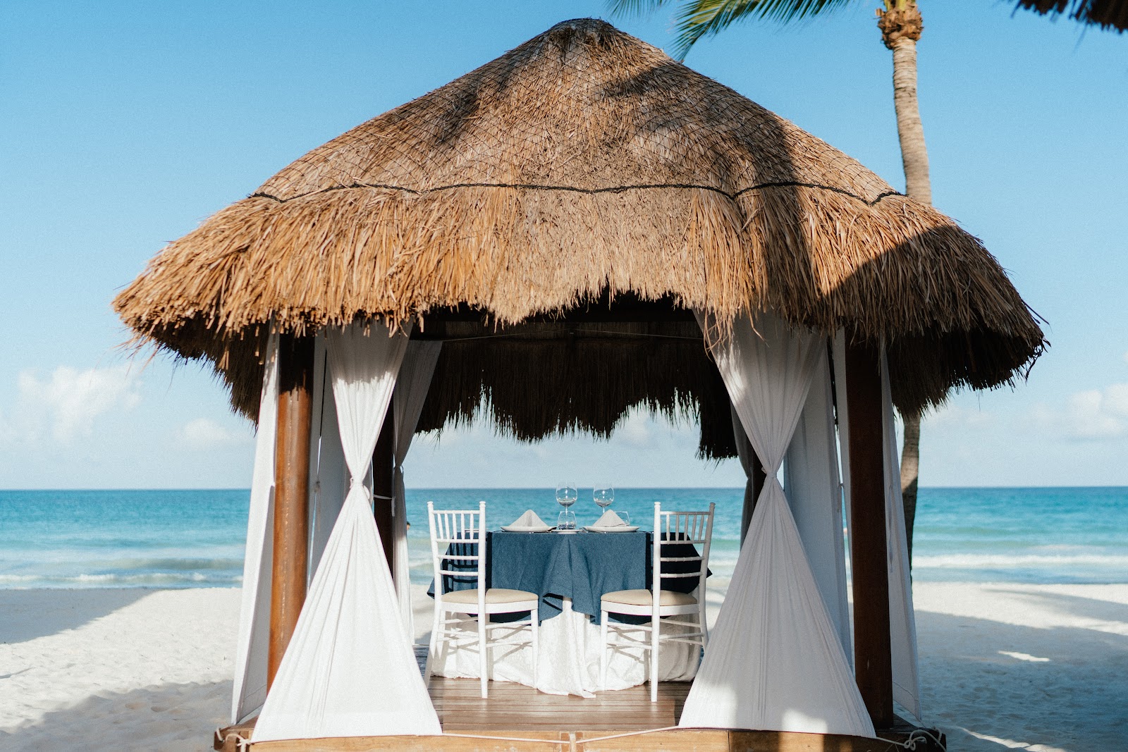 Thatched-roof beachfront cabana at Secrets Maroma Beach Riviera Cancun with a table set for two overlooking the Caribbean Sea.