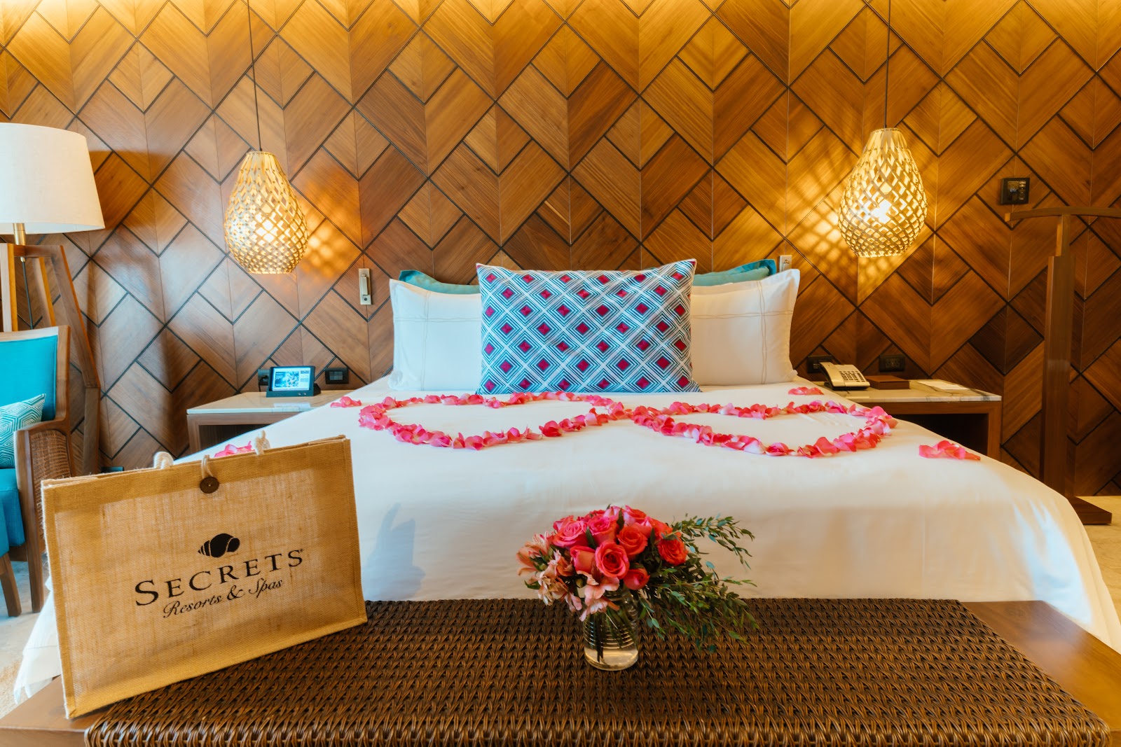 Secrets Maroma Beach Riviera Cancun bedroom with herringbone wood accent wall, bed decorated with rose petals, and hanging woven pendant lights.