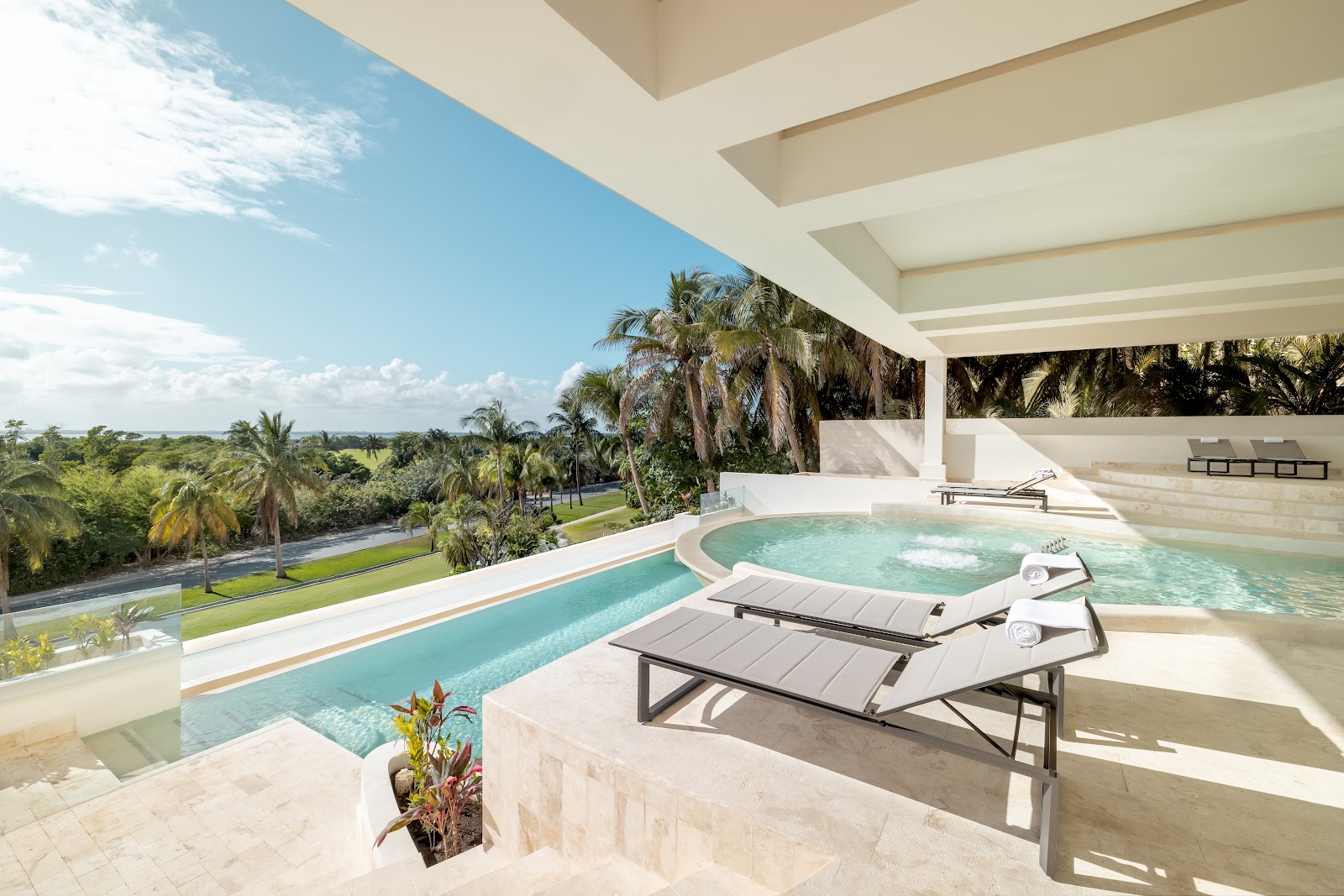 Lounge chairs sit on a terrace beside a curved pool and hot tub at Secrets Mirabel Cancun, with palm trees and tropical grounds visible beyond.