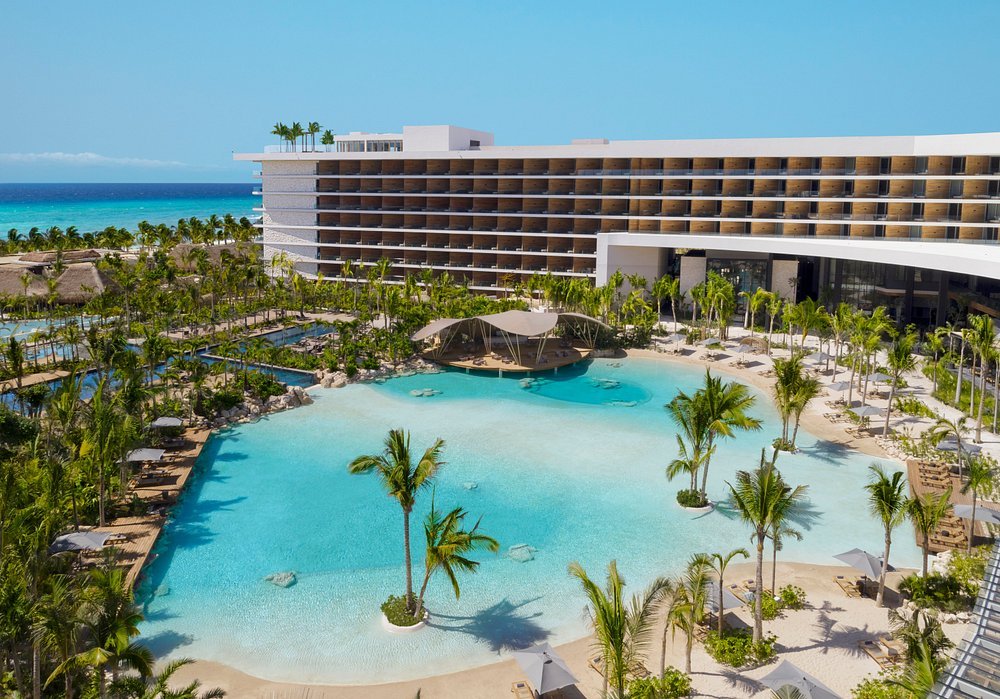 Large turquoise pool with palms and resort buildings beside the sea at Secrets Moxché.