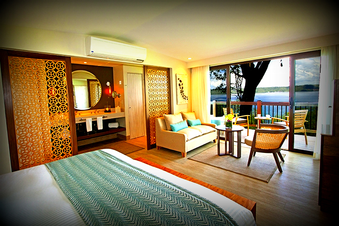 Modern resort room at Secrets Papagayo with wood furnishings, geometric patterns, and glass doors opening to a balcony overlooking a bay.