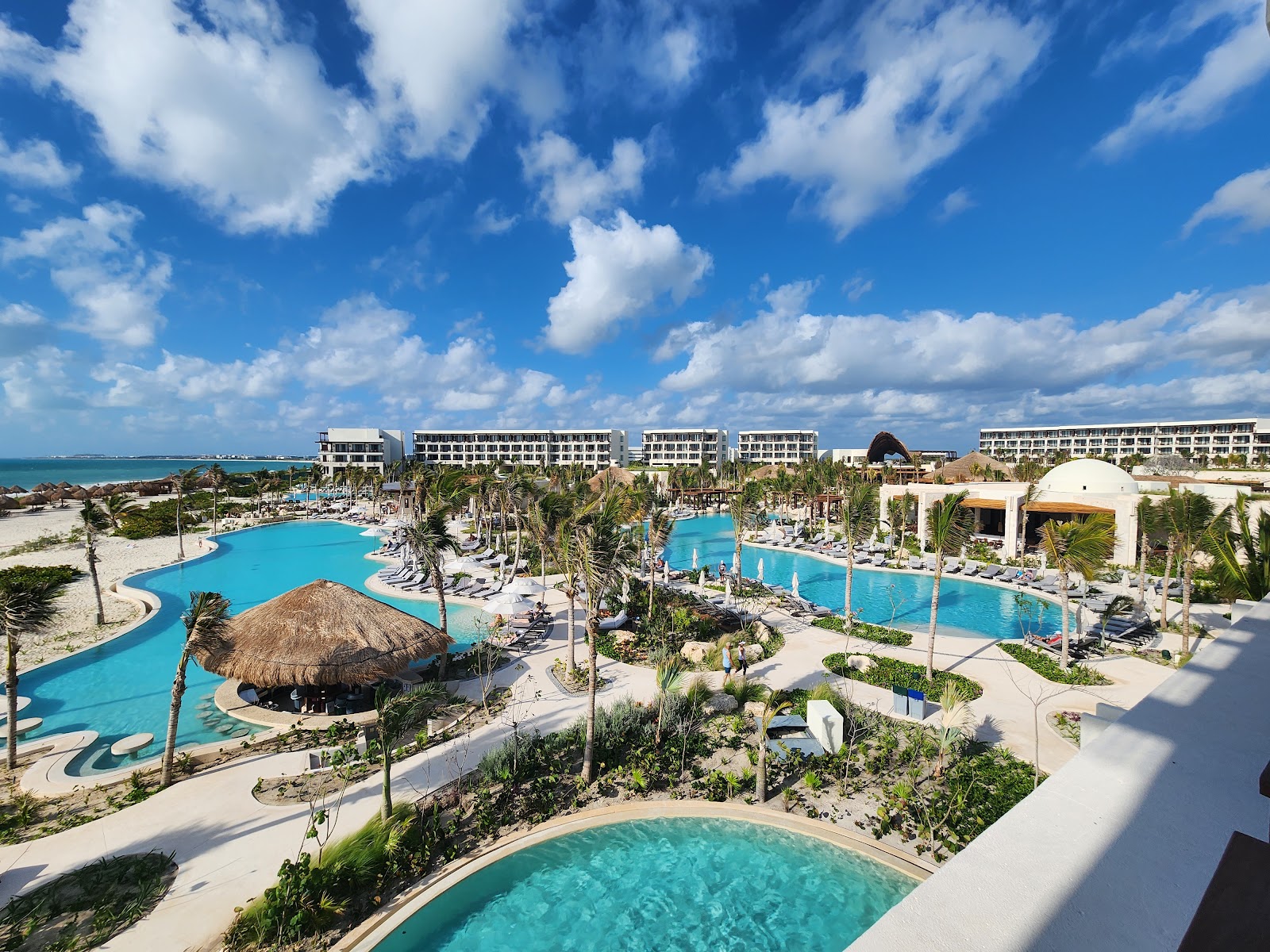 Aerial view of Secrets Playa Blanca Costa Mujeres with multiple turquoise pools, white resort buildings, palm trees, and Caribbean Sea under blue sky.