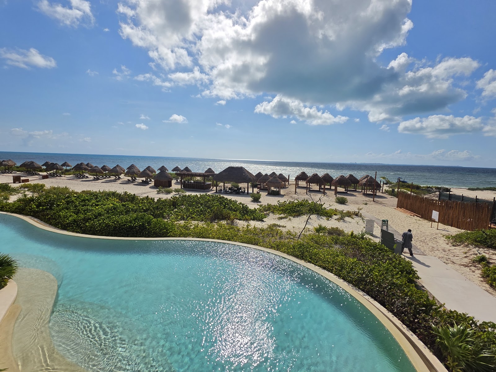 Turquoise pools surrounded by lush tropical vegetation and palm trees at Secrets Playa Blanca Costa Mujeres, with a shaded lounge area in foreground.