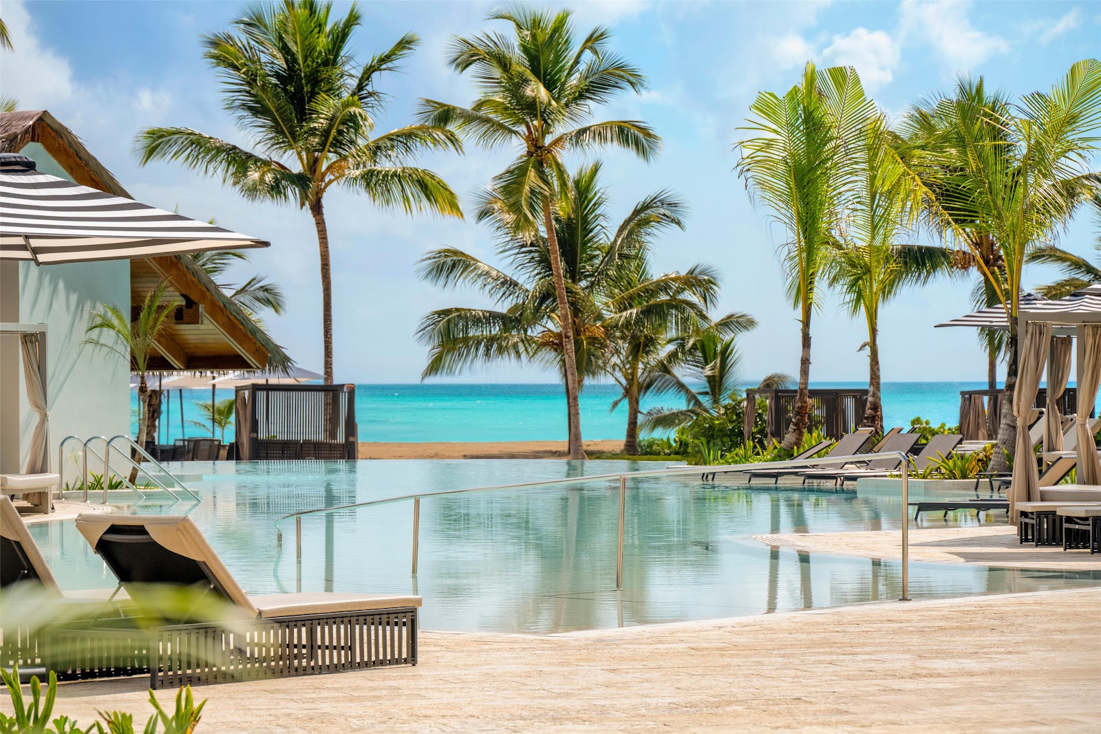 Infinity pool overlooking turquoise ocean and beach at Secrets Playa Esmeralda, surrounded by palm trees and cabanas.