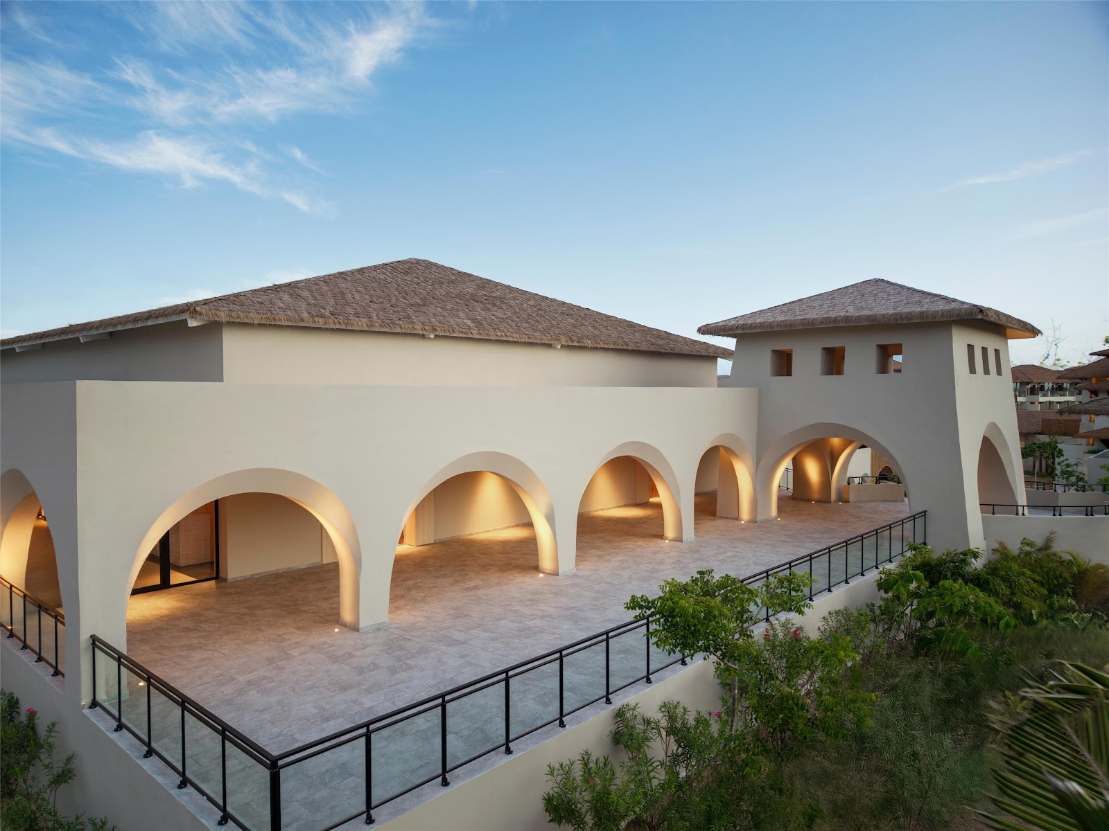 White building with thatched roofs and large rounded archways at Secrets Playa Esmeralda Resort & Spa, lit from within at dusk.