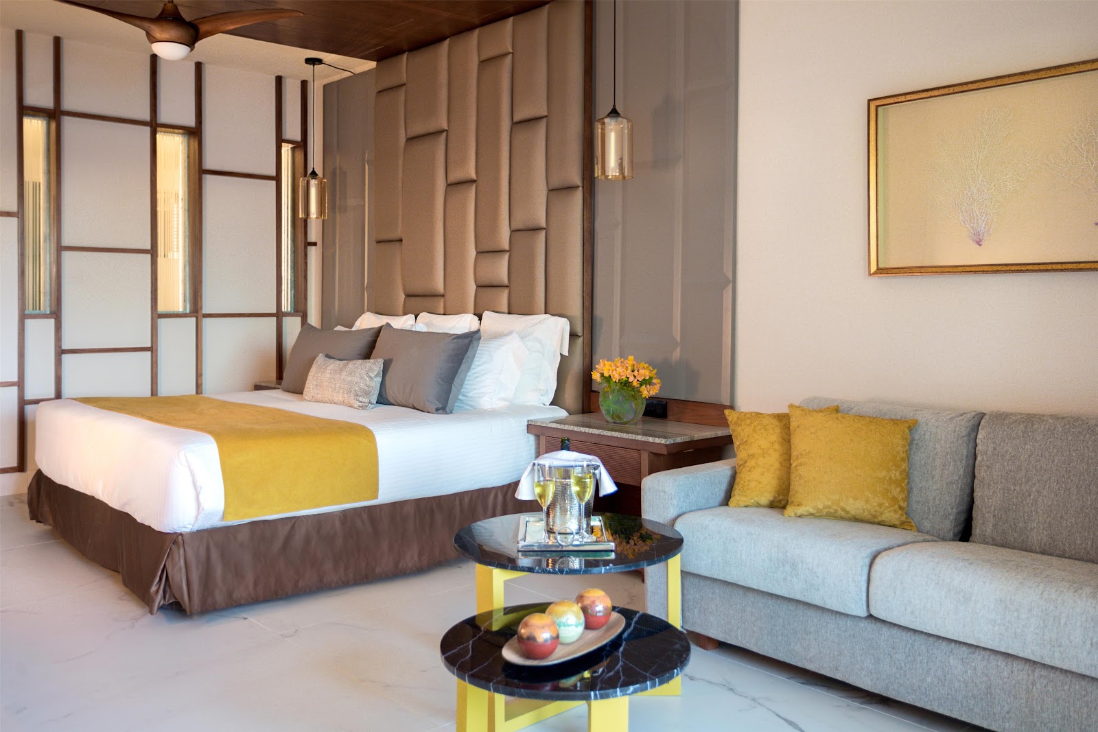 Modern resort room with king bed, work desk, black marble table with white flowers, dark wood accents, and mirrored bathroom entrance.