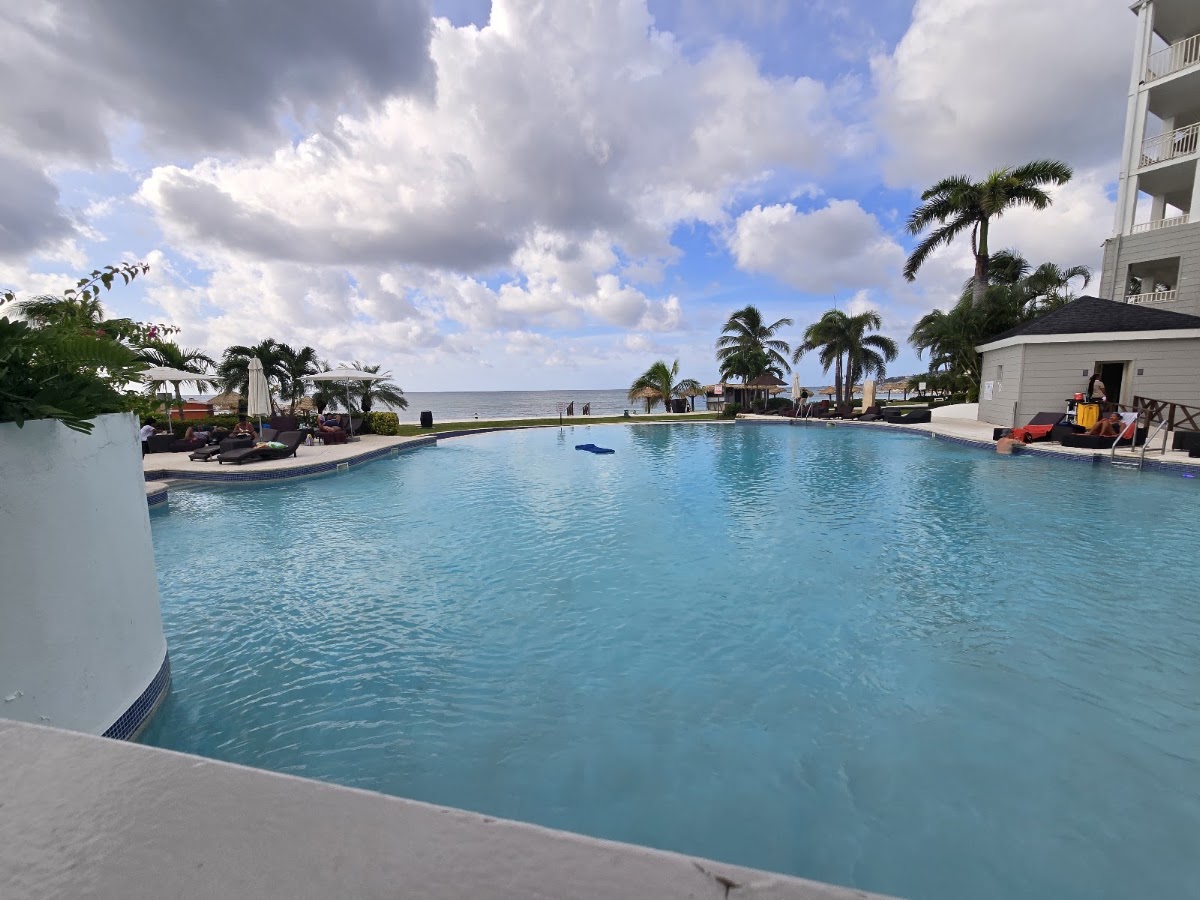 Large resort pool with turquoise water, palm trees, lounge chairs, and ocean view beyond at Secrets St. James Montego Bay.
