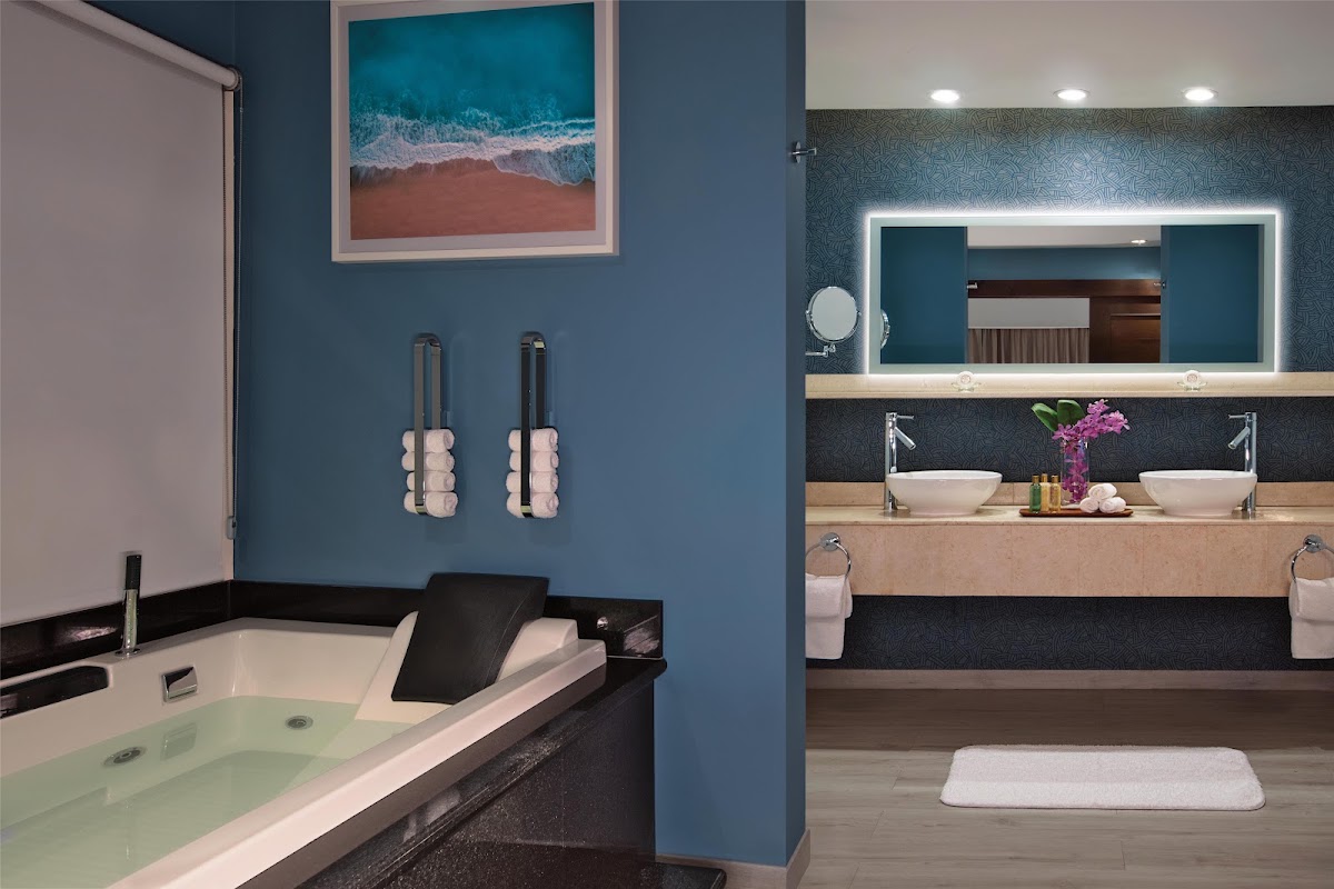 Modern bathroom with soaking tub, heated towel racks, and dual vanity with illuminated mirror and pink flowers at Secrets St. James Montego Bay.