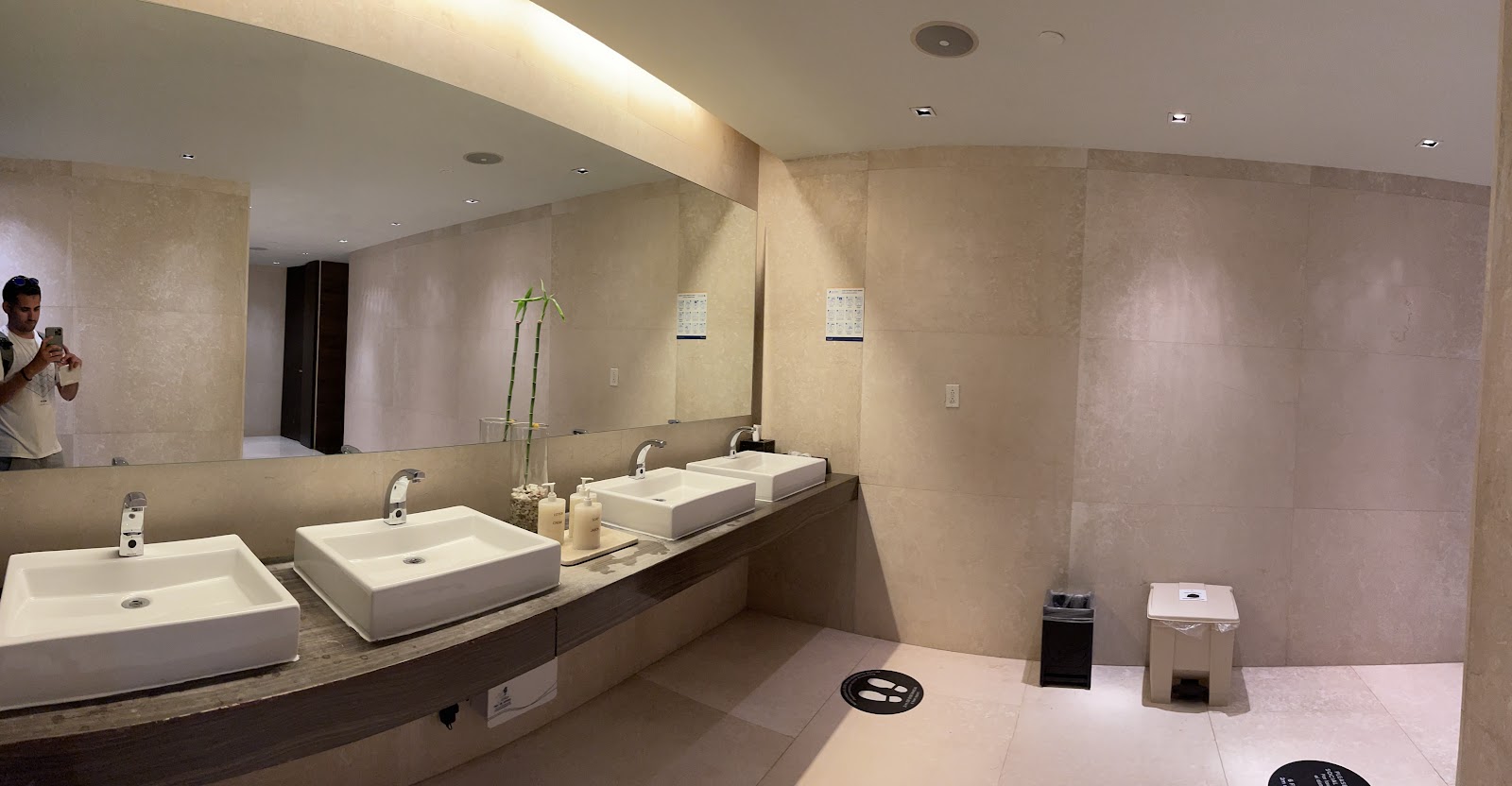 Modern bathroom with multiple white vessel sinks, neutral tile walls, and a large mirror at Secrets The Vine Cancun.