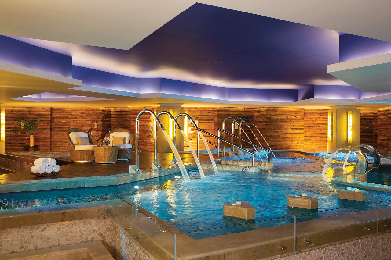 Indoor pool at Secrets Vallarta Bay with wooden walls, metal railings, lounge chairs, and purple-lit ceiling in Puerto Vallarta.
