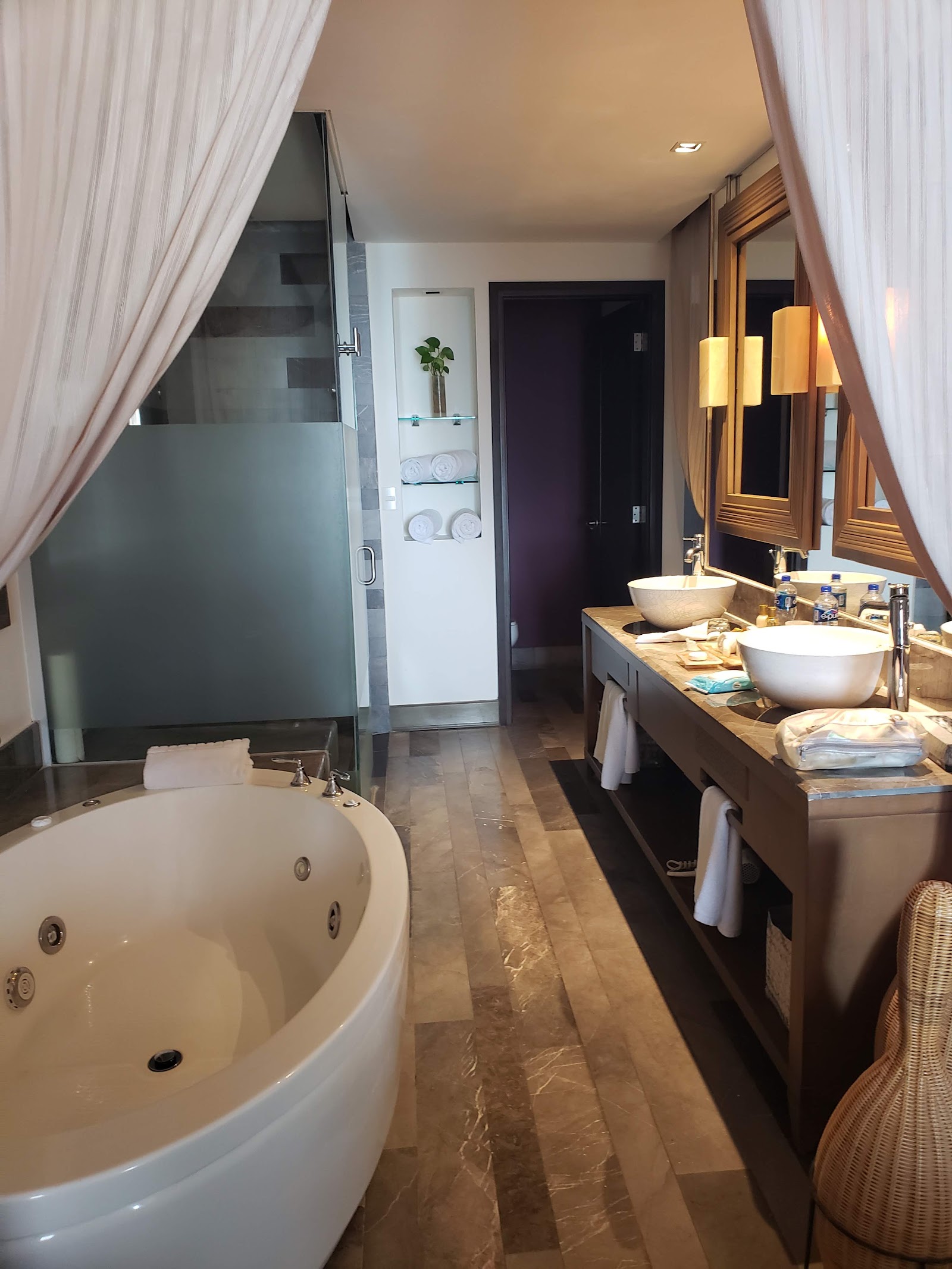 Spacious bathroom with round soaking tub on left, dual vanity with vessel sinks, glass-enclosed shower, and warm lighting at Secrets Vallarta Bay.