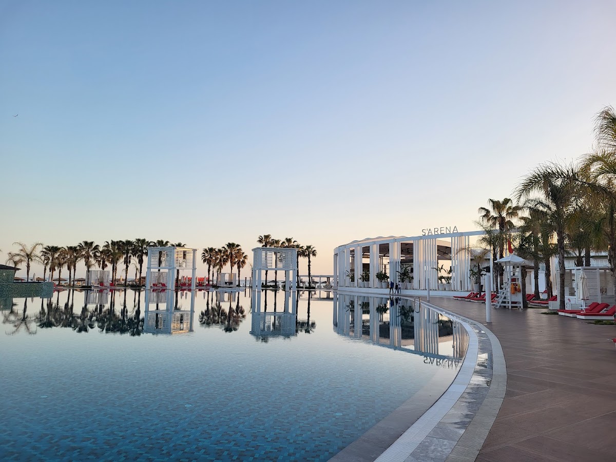 Sarena restaurant and pool area at Selectum Luxury Resort Belek with palm trees and clear water reflections at dawn.