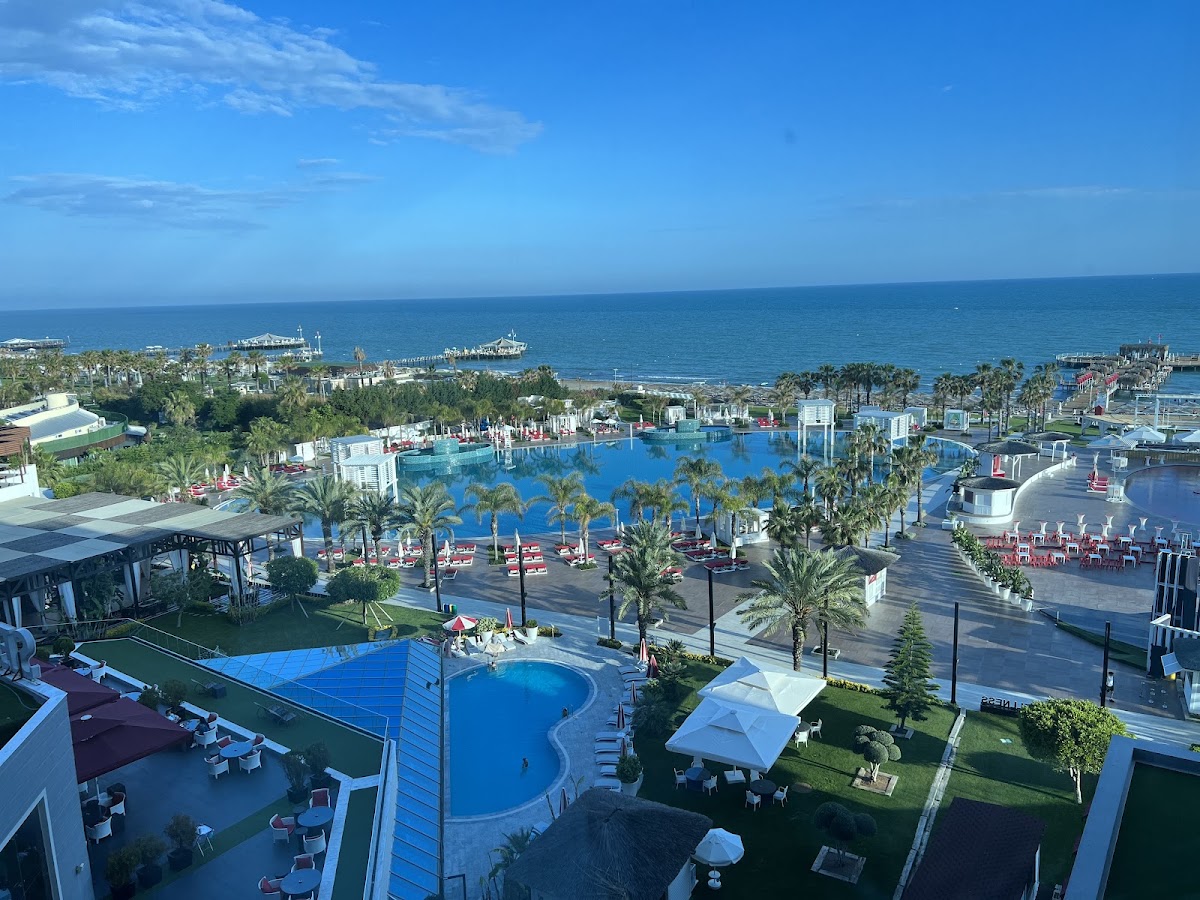 Aerial view of Selectum Luxury Resort Belek's sprawling pool complex with blue water, palm trees, and Mediterranean Sea beyond.