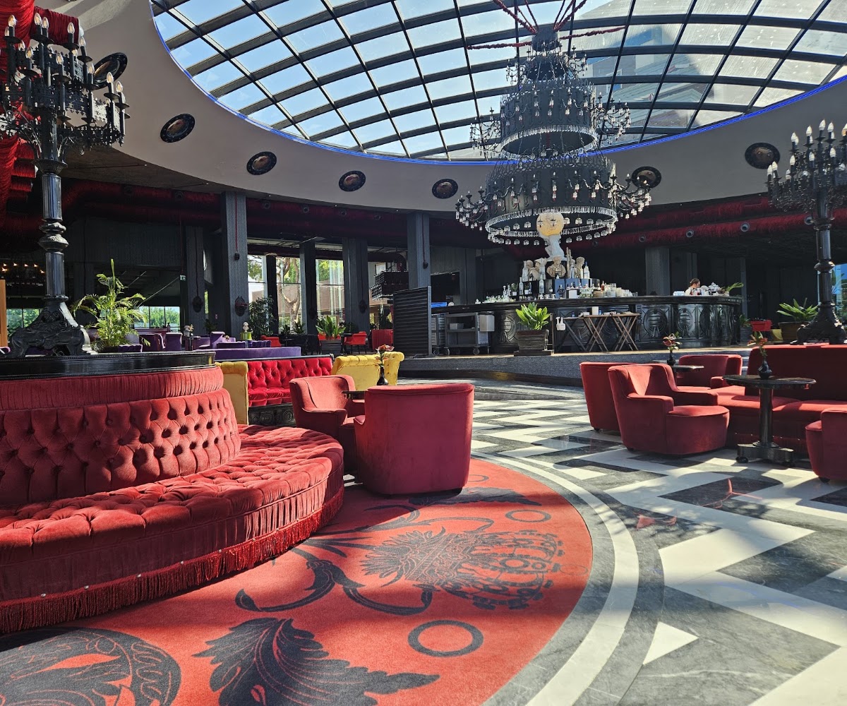 Selectum Luxury Resort Belek's lobby lounge features red tufted seating, ornate chandeliers, a glass ceiling, and decorative patterned flooring.