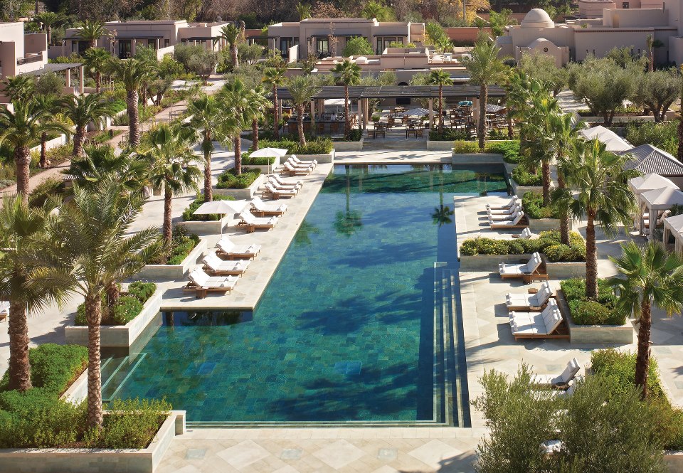 Resort pool surrounded by palm trees with lounge chairs and desert buildings in the background.