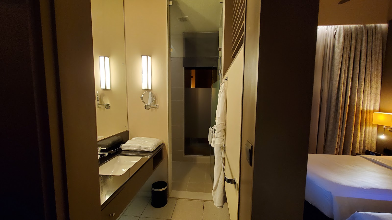 Modern bathroom with double vanity, illuminated mirrors, walk-in shower, and folded towels, adjoining a guest room.