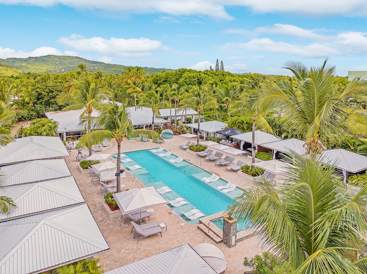 Turquoise pool surrounded by lounge chairs and white umbrellas at Serenity at Coconut Bay, with palm trees and lush green hills beyond.