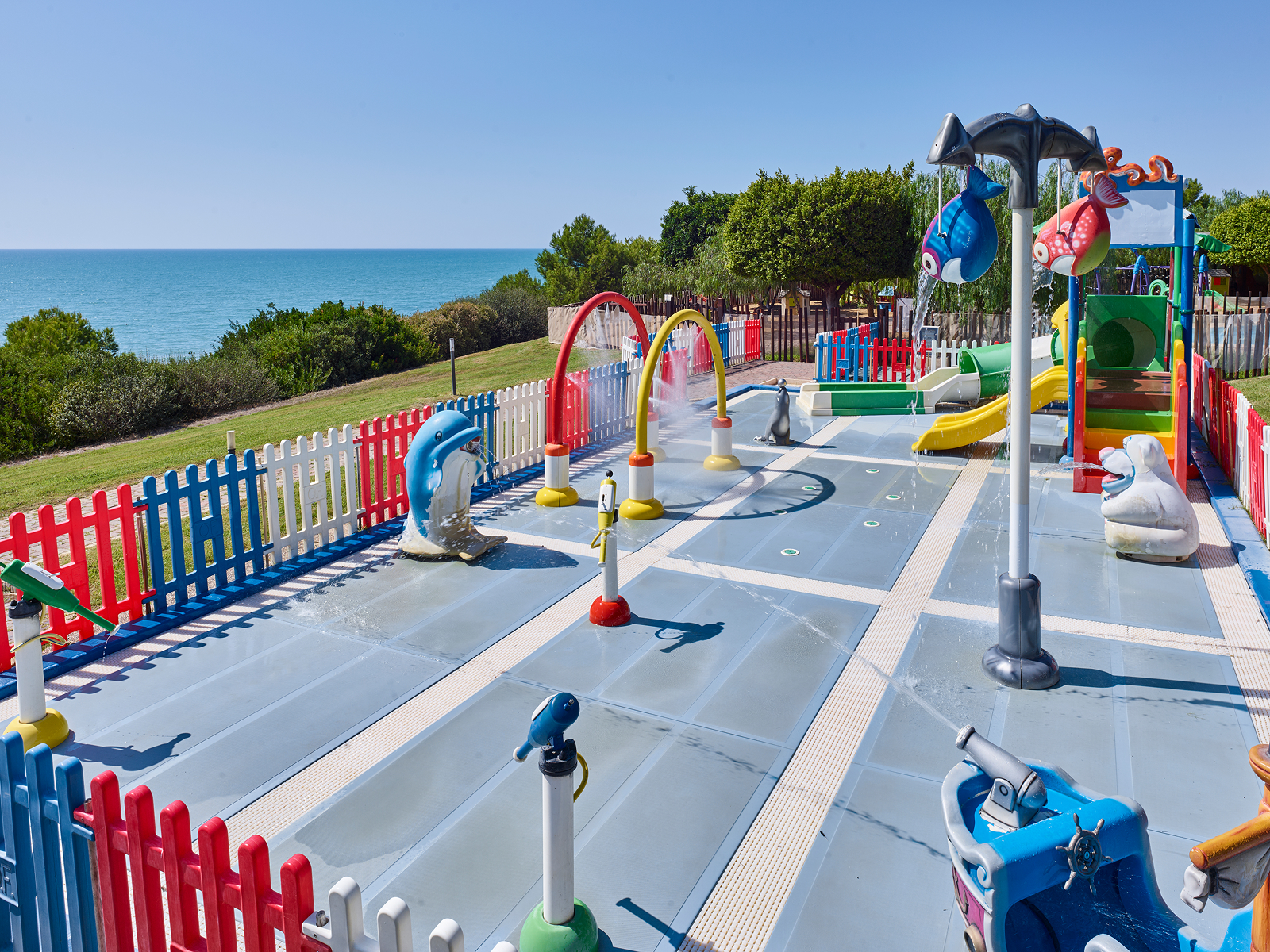 Colorful children's playground with slides, climbing structures, and water features overlooking the sea at Serenusa Resort.