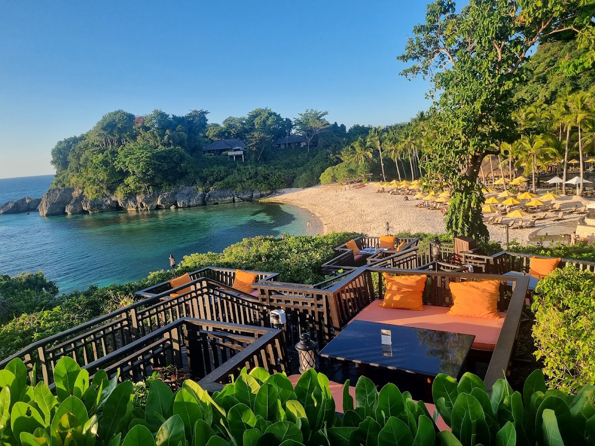Wooden deck with orange cushioned seating overlooks a sandy beach, turquoise water, and jungle-covered cliff at Shangri-La Boracay.