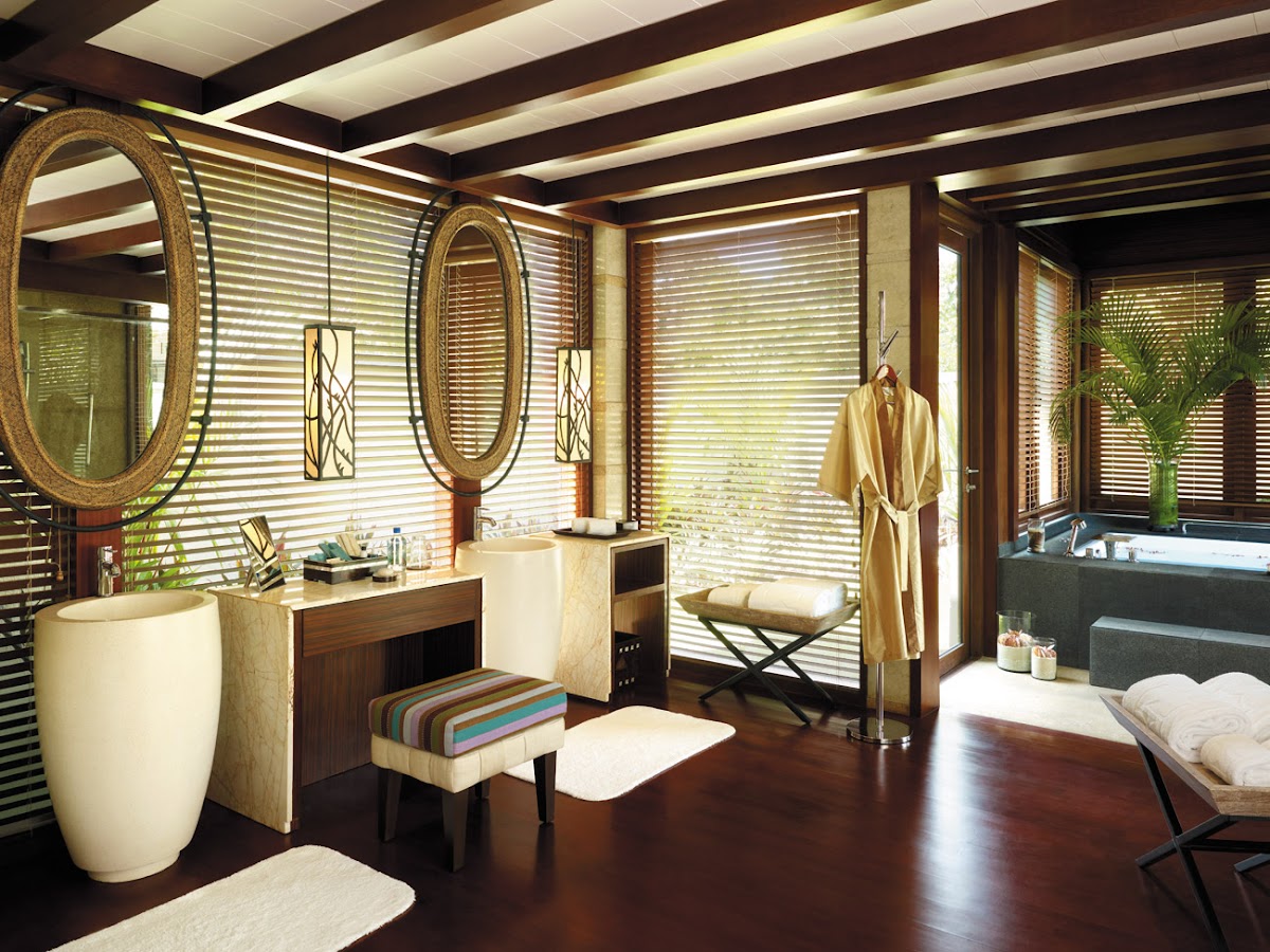 Spa bathroom with dual vanities, large oval mirrors, louvered screens, soaking tub, and dark wood flooring.