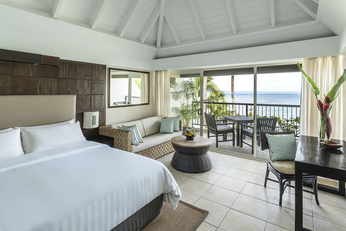 Spacious beachfront suite with king bed, sitting area, and ocean view from balcony at Shangri-La Yanuca Island.