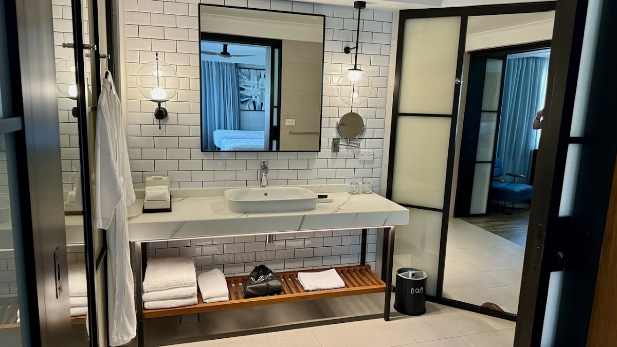 Modern bathroom at Sheraton Fiji Golf & Beach Resort with white subway tile walls, floating vanity with vessel sink, mirrored cabinet, and wooden shelf holding rolled towels.