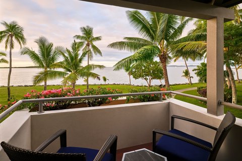 A covered balcony with wicker chairs overlooks palm trees, manicured lawns, and ocean views at Sheraton Fiji Golf & Beach Resort.