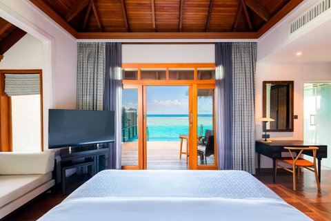Bright bedroom with wooden ceiling, twin beds, and orange-framed doors opening to turquoise ocean at Sheraton Maldives Full Moon Resort & Spa.