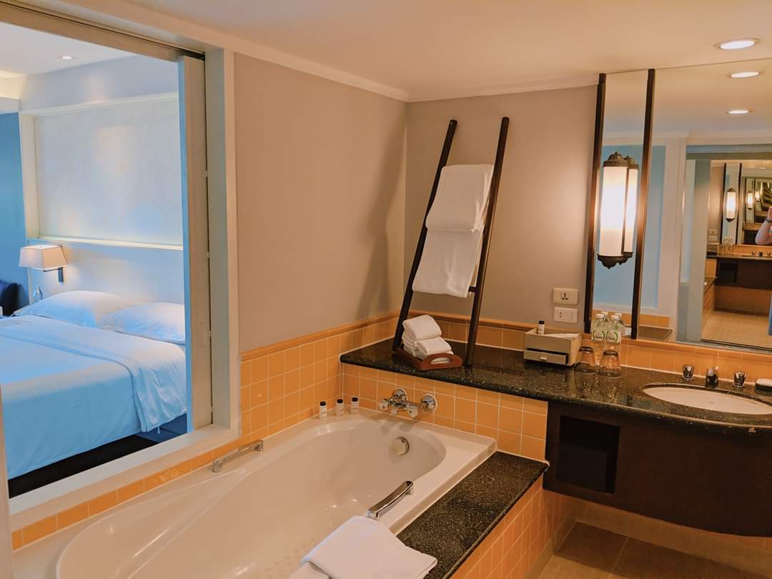 Bathroom with orange tile surround, soaking tub, double vanity with dark countertop, and view into bedroom with blue bedding through open doorway.