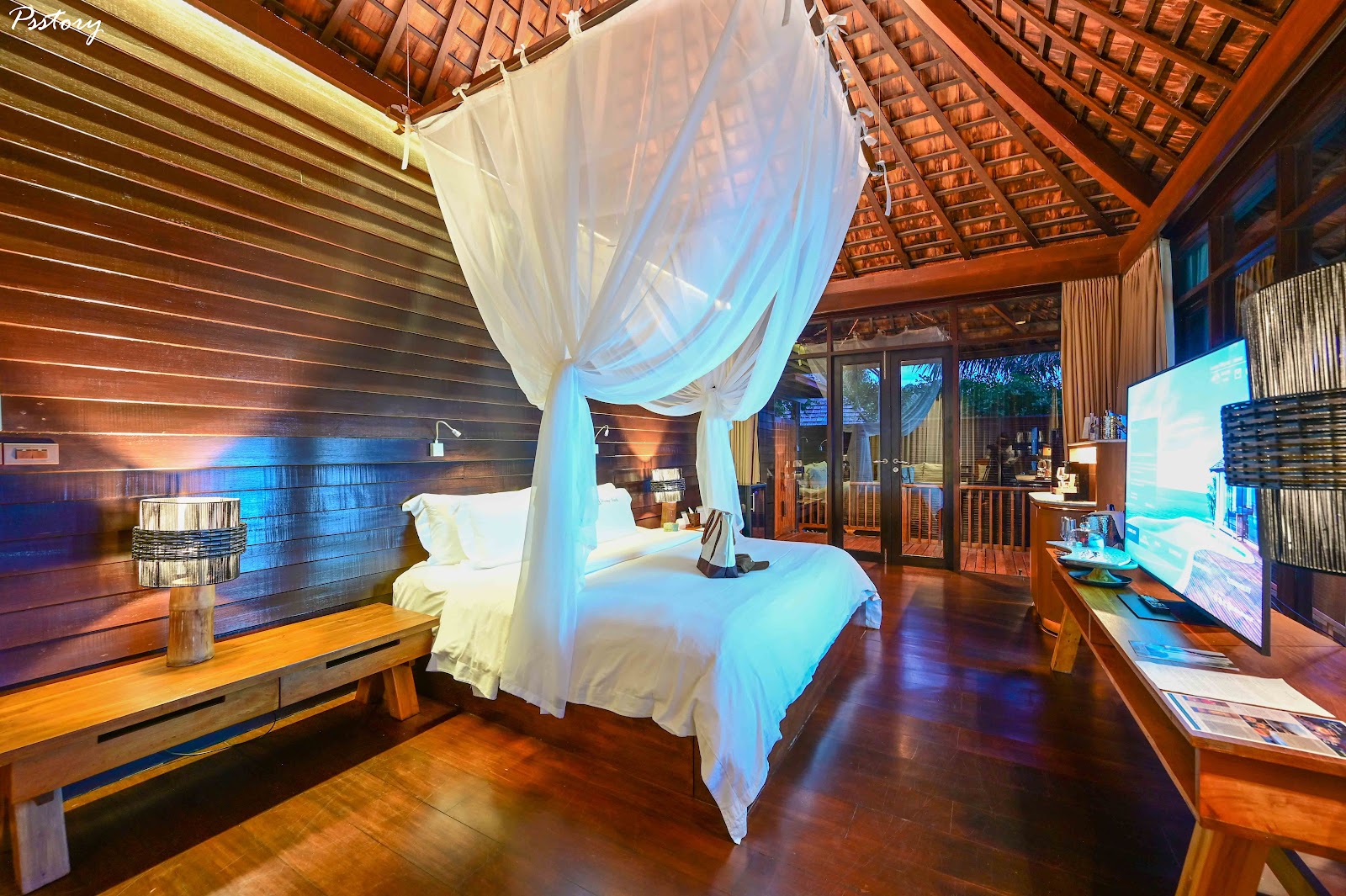 Canopy bed with white drapes in wooden bungalow bedroom with thatched roof and ocean view doors at Silavadee Pool Spa Resort.