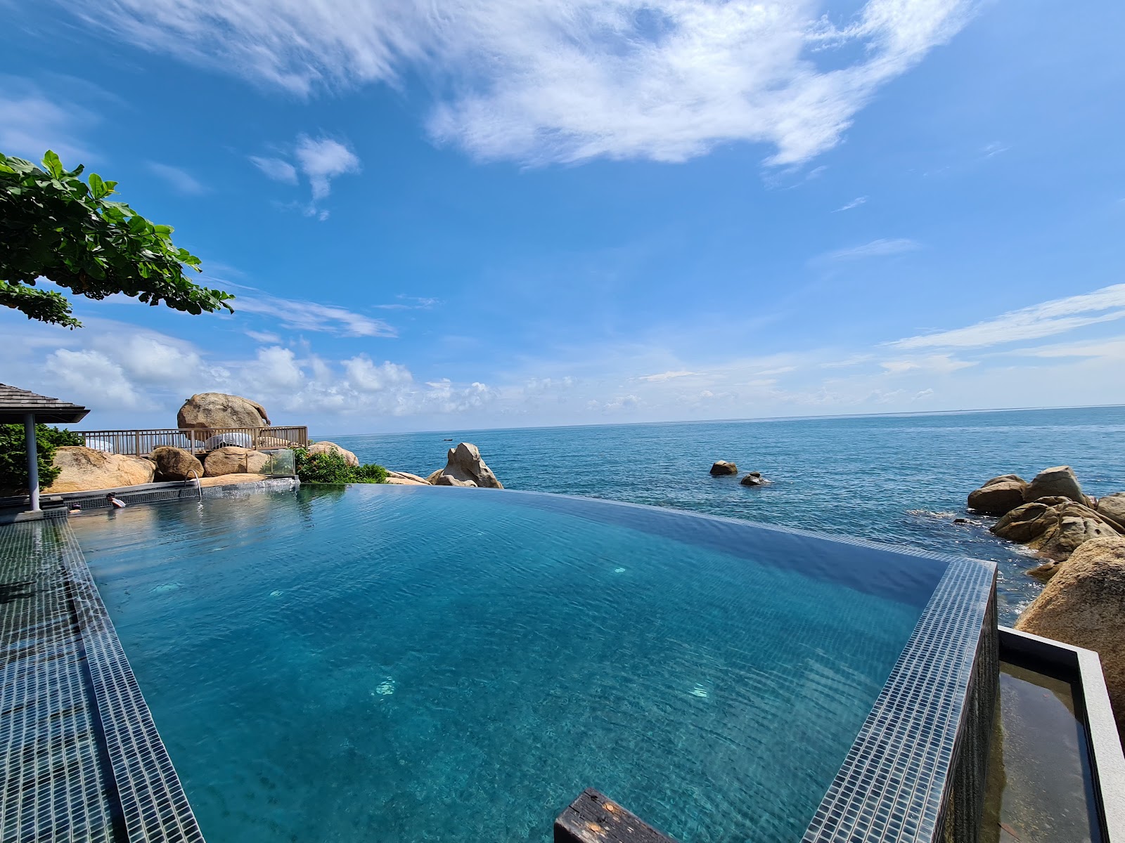 Infinity pool with teak decking overlooks turquoise ocean and rocky outcrops at Silavadee Pool Spa Resort.