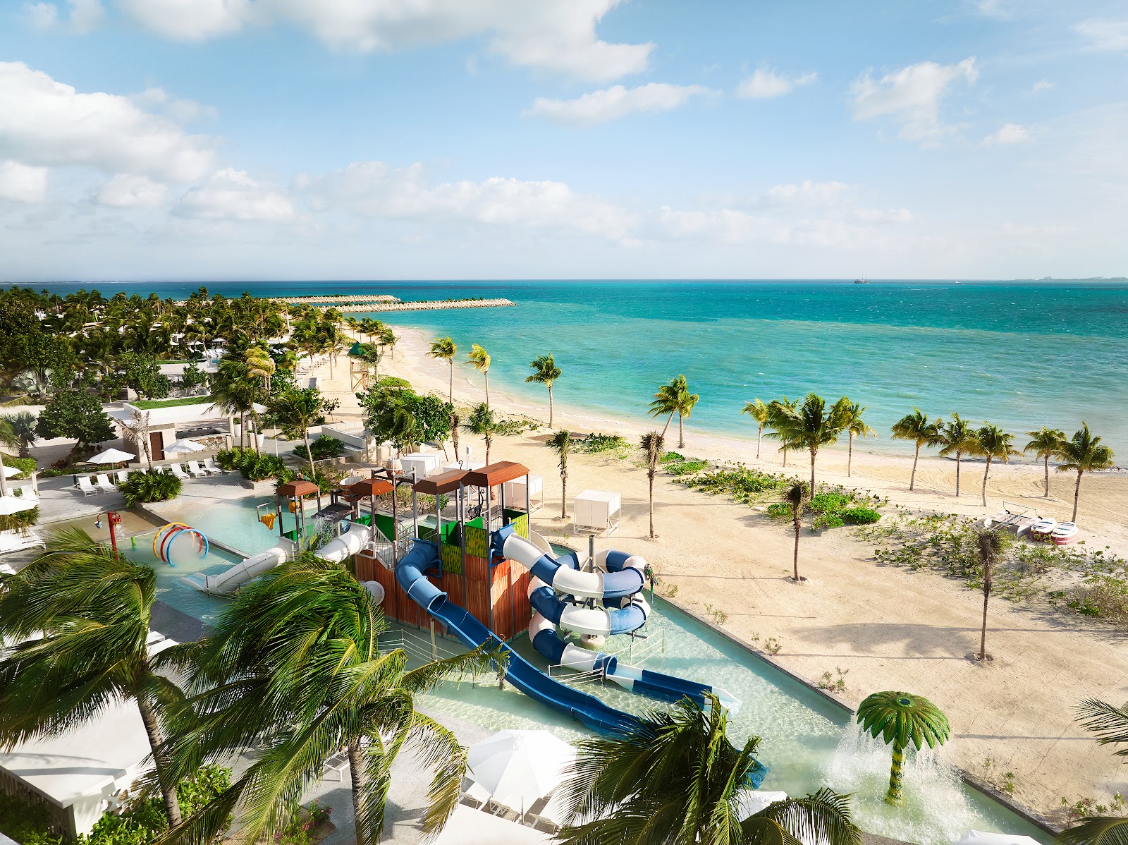 SLS Playa Mujeres waterpark with blue slides overlooking a sandy beach and turquoise Caribbean Sea dotted with palm trees.