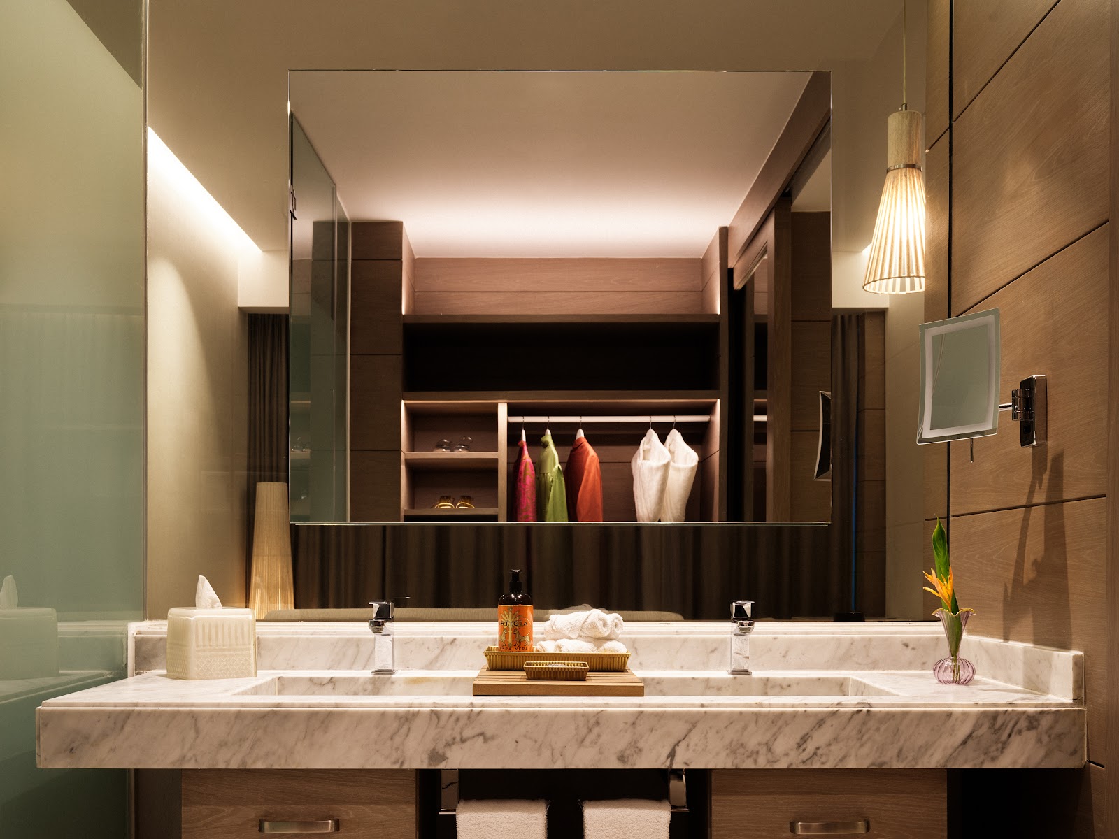 Marble vanity with two sinks, amenities, and a large illuminated mirror backed by wood cabinetry and shelving at SLS Playa Mujeres.